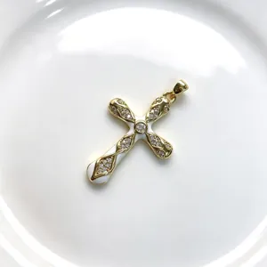 Vue détaillée d'un pendentif croix dorée en émail blanc et oxydes de zirconium.