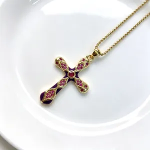 Détail en gros plan du pendentif en forme de croix dorée avec émail violet et zircons rouges.