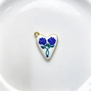 Close-up of a heart-shaped enamel pendant featuring blue rose patterns and a polished gold rim.