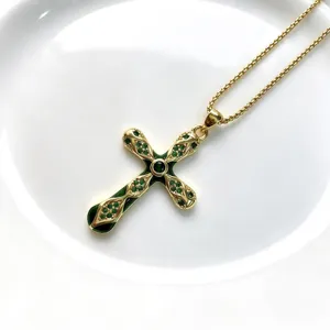 Vue de détail en gros plan d'un pendentif croix doré avec émail vert et pierres de zircone cubique brillantes.