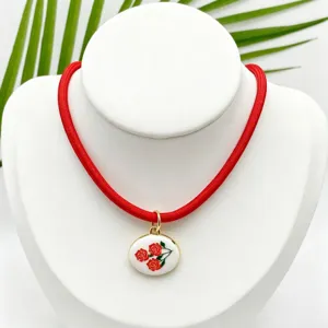 Detalle de collar de cordon rojo con colgante ovalado floral esmaltado estilo retro.