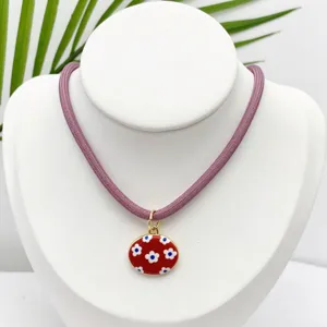 Primer plano detallado del collar con colgante ovalado vintage y patrón floral rojo.
