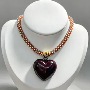 Close-up details of the brown braided rope necklace featuring a glossy dark red heart pendant.