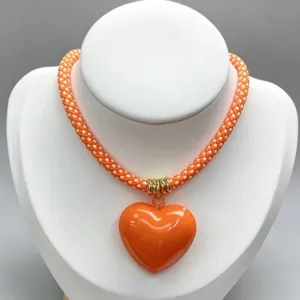 Orange braided necklace with glossy heart pendant fashion jewelry accessory details.
