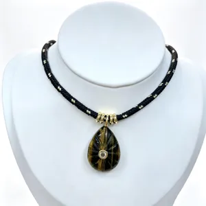 Close-up detail of teardrop carved gemstone pendant with central zircon on black braided necklace.