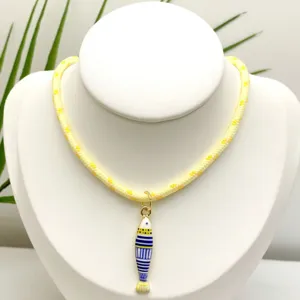 Gros plan détail du collier pendentif poisson rayé style marin avec chaîne tressée jaune.