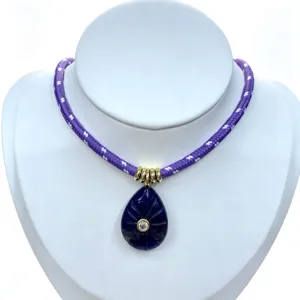 Close-up of the carved deep blue teardrop gemstone pendant with zircon and gold rings on purple cord.