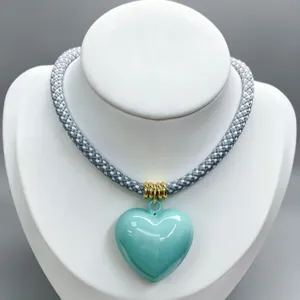 Stylish braided cord necklace featuring a glossy light blue heart pendant and gold rings.