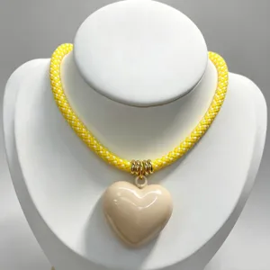 Detail view of the yellow woven rope necklace featuring a glossy beige heart pendant.