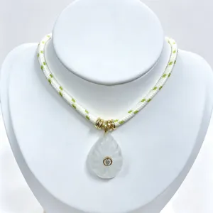 Detailed view of carved crystal teardrop pendant necklace with gold rings and woven rope.