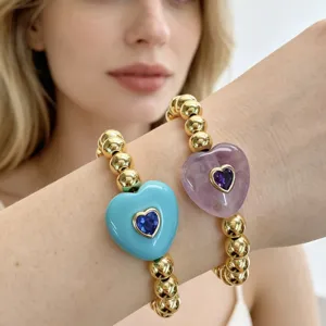 Nahaufnahme von goldenen Perlenarmbändern mit bunten Herzanhängern und Zirkonbesatz am Handgelenk.