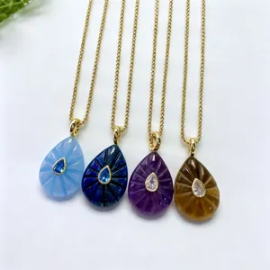 Detailed view of four colorful carved teardrop gemstone pendant necklaces with gold chains.