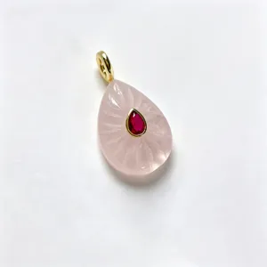 Detail view of teardrop rose quartz pendant with carved sunburst pattern and red center stone.