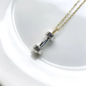 Gros plan détail du collier pendentif haltère avec lettrage gravé et cristaux étincelants.