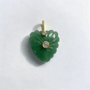 Detailed close-up of a carved green natural stone heart pendant with gold-tone accents and stones.