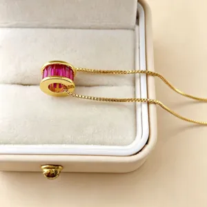 Gedetailleerde close-up van een vergulde cilindrische hanger met sprankelende roze zirkonia.