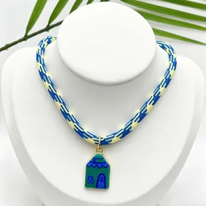 Close-up detail of a handmade blue and yellow woven rope necklace with a cute green house pendant.