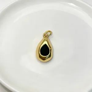 Close-up detail of glossy gold teardrop pendant with black inset on white plate background.
