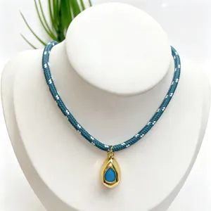 Close-up detail of the gold teardrop gemstone pendant on a blue braided rope necklace.