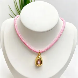 Close-up detail of pink braided rope necklace with gold teardrop gemstone pendant fashion.