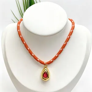 Close-up detail of orange white braided rope necklace with gold teardrop red gem pendant.