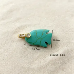 Close-up detail of a turquoise fish pendant with gold diamond bail on sand background.