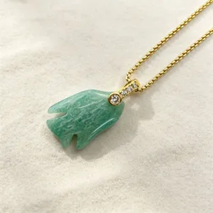 Stunning close-up detail of the green crystal fish pendant necklace displayed on sand.