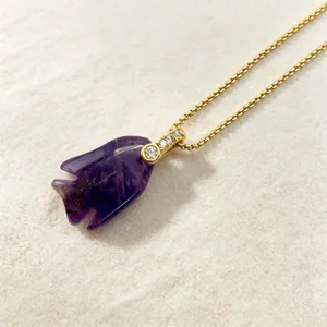 Close-up detail of carved purple crystal fish pendant with sparkling diamond gold connector.