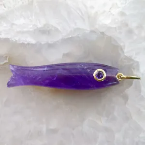 Primo piano di un ciondolo a forma di pesce in ametista naturale con occhiello dorato.