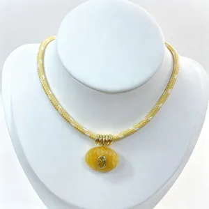 Primo piano dettagliato della collana in corda intrecciata gialla con ciondolo ovale e anelli d'oro.