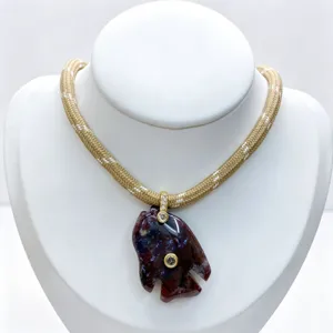Close-up detail of carved stone fish pendant necklace with zircon and woven cord.