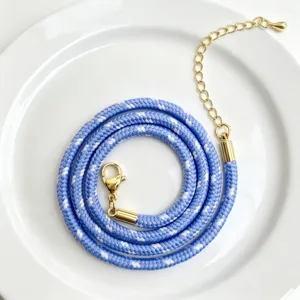 Detailaufnahme der blau-weißen geflochtenen Kordelkette mit goldenem Karabinerverschluss.
