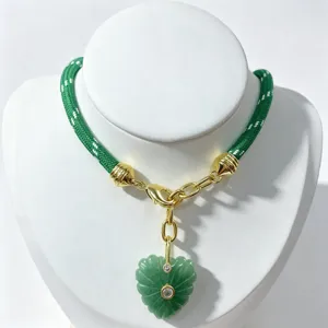 Green braided cord necklace detail featuring gold clasp and carved heart gemstone pendant.