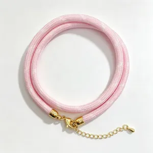 Detail shot of pink woven round rope necklace with golden metal clasp and extension chain.