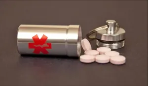 Detail view of the portable aluminum emergency pill capsule container with keyring and pink pills.