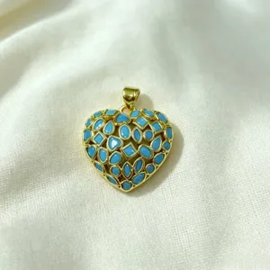 Close up detail of gold plated heart pendant inlaid with blue stones on white fabric backdrop.