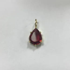 Dettaglio ciondolo goccia zircone rosso, primo piano accessorio gioiello dorato.