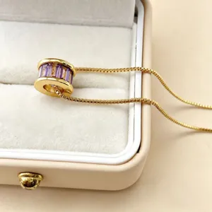 Gedetailleerde close-up van de elegante vergulde cilindrische hanger met paarse stenen.