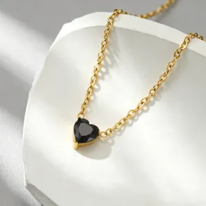 Close-up detail of the elegant black heart gemstone pendant on a refined gold chain necklace.