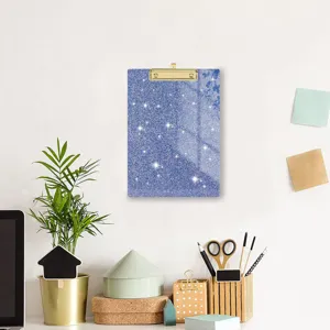 Gedetailleerd overzicht van blauw glitter acryl klembord met gouden clip op bureau.