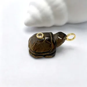 Gros plan détaillé du pendentif tortue en pierre naturelle sculptée avec anneau doré et cristal.