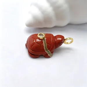Gros plan détaillé d'un pendentif tortue sculpté en pierre rouge naturelle avec anneau doré.