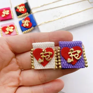 Handcrafted fabric square pendant detail featuring red heart and gold letter Fe charm.