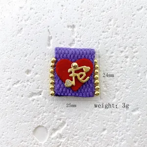 Close-up detail shot of handmade woven square purple fabric charm with gold letter and beads.