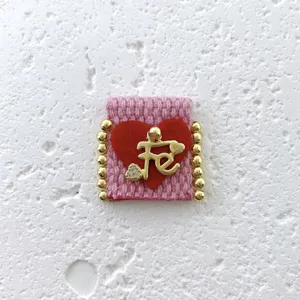 Close-up detail of handmade pink woven fabric charm with red heart and gold Fe letter.