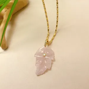 Gros plan détaillé du collier pendentif feuille en cristal rose sculpté avec chaîne dorée.