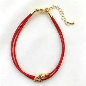 Dettaglio in primo piano del bracciale intrecciato in corda rossa multistrato con perline d'oro.