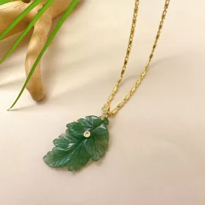 Gros plan détaillé d'un collier pendentif feuille verte sculptée avec pierre brillante.