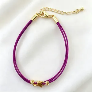 Primo piano dettagliato di un bracciale in corda intrecciata viola con ciondoli farfalla.