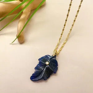 Gros plan détaillé d'un magnifique collier pendentif feuille sculptée chaîne dorée.